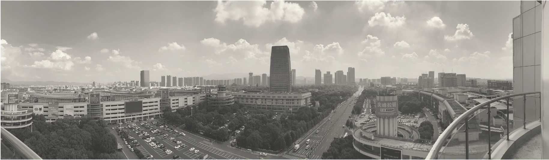 Yiwu- Vista panorámica de un paisaje urbano con edificios modernos, carreteras y estacionamientos bajo un cielo nublado, capturado en blanco y negro, ideal para Compras en China.