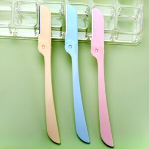 Hola Yiwu- El Kit 3 perfiladores de cejas - AGE-334 incluye tres afeitadoras faciales plegables en colores pastel (melocotón, azul, rosa), mostradas sobre una superficie verde con un estuche de plástico transparente detrás de ellas.